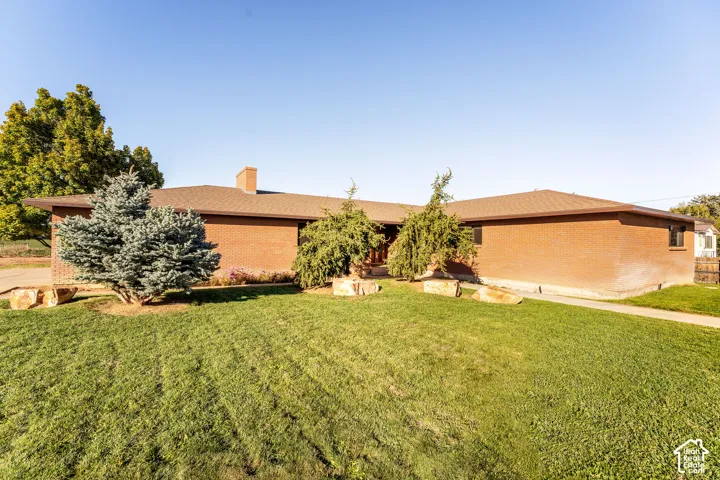 Single-story brick exterior featuring a low-pitch roof, chimney, and landscaped lawn with mature trees and natural stone accents