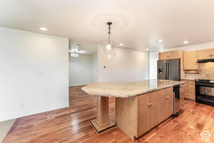 Kitchen featuring wood-finish flooring, a central island with stone countertop, wood cabinetry, stainless steel appliances, and a glass globe pendant light