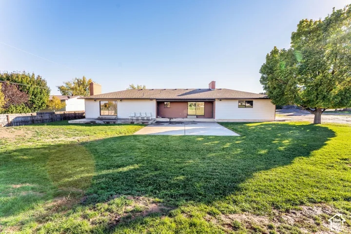 Single-story exterior featuring a concrete patio, dual brick chimneys, and an expansive lawn