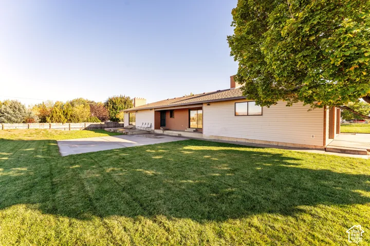 Exterior featuring light-toned horizontal siding, brick accent walls, a concrete patio, and a expansive lawn with mature trees