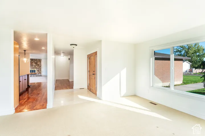 Solid wood entry door with glass sidelights, large picture window, neutral carpeting, and wood-finish flooring