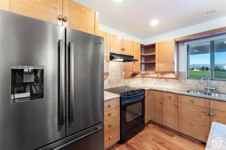 Kitchen featuring wood cabinetry, stone countertops, stone tile backsplash, stainless steel refrigerator, and wood-finish flooring