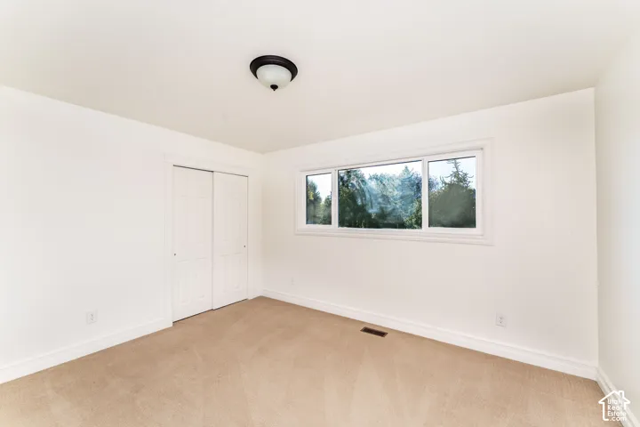 Neutral interior space featuring wall-to-wall carpeting, dual-panel sliding closet doors, a wide horizontal window with casing, and a ceiling-mounted light fixture