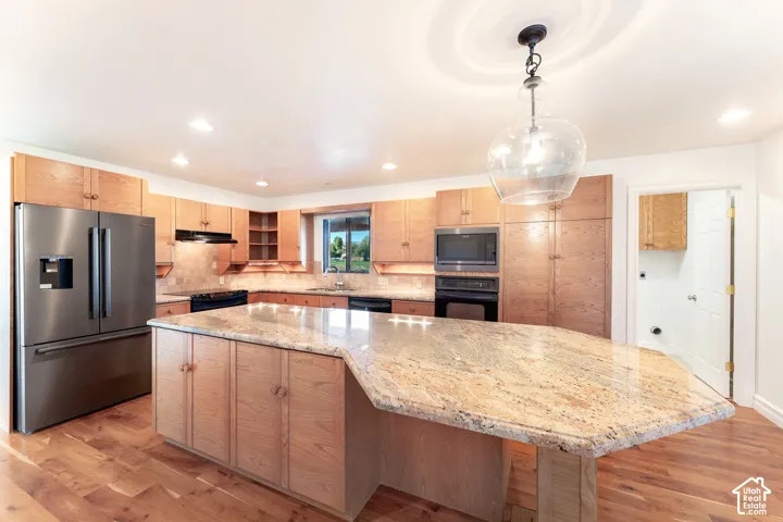 Kitchen featuring a large island with stone-surface countertop, wood-finish cabinetry, stainless steel appliances, and wood-finish flooring