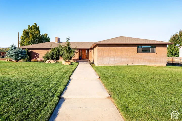Single-story brick exterior featuring a hip roof, chimney stack, concrete walkway, and expansive front lawn