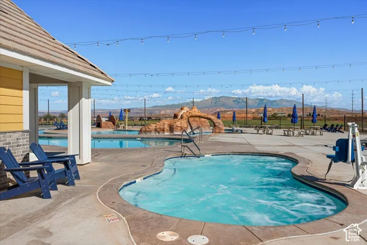 Outdoor pool area featuring a spa, rock-feature water element, concrete decking, and overhead string lighting against a mountain backdrop