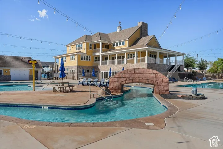 Swimming pool complex featuring a stone-accented arched bridge, concrete decking, multi-level exterior structure with covered patios, and overhead string lighting