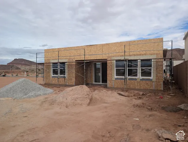 Single-story residential structure under construction featuring oriented strand board exterior sheathing, installed white-framed windows, and desert mountain backdrop