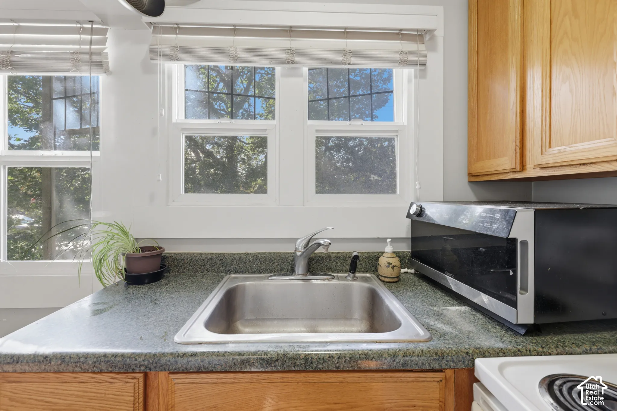 Kitchen area featuring natural wood cabinetry, stone-texture countertops, a stainless steel undermount sink with a pull-out sprayer faucet, and dual windows