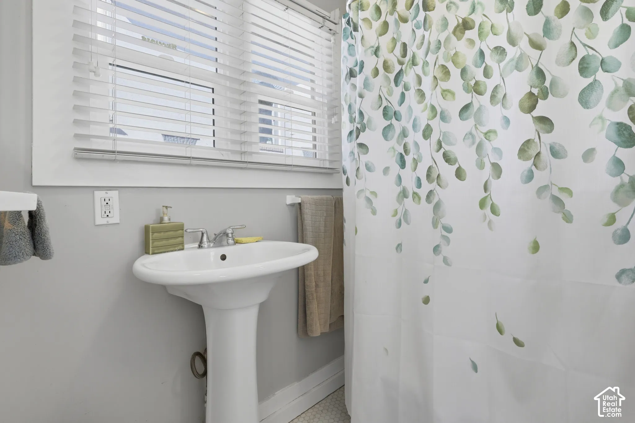 White pedestal sink with a dual-handle chrome faucet and horizontal slat window blinds
