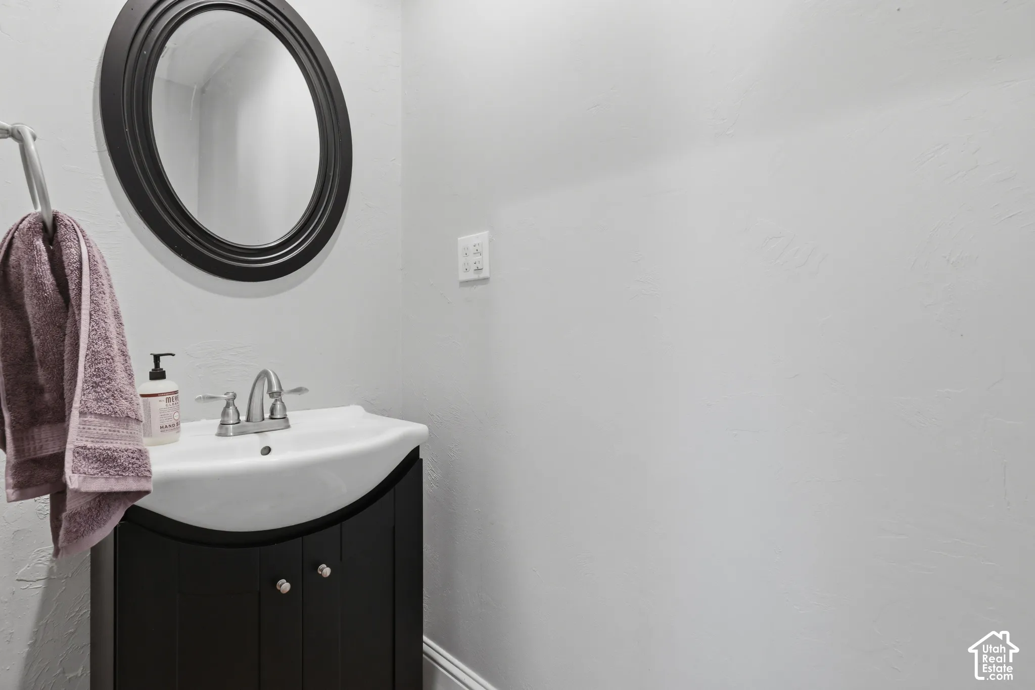 Curved black vanity cabinet with an integrated white sink, polished chrome dual-handle faucet, and matching oval wall mirror