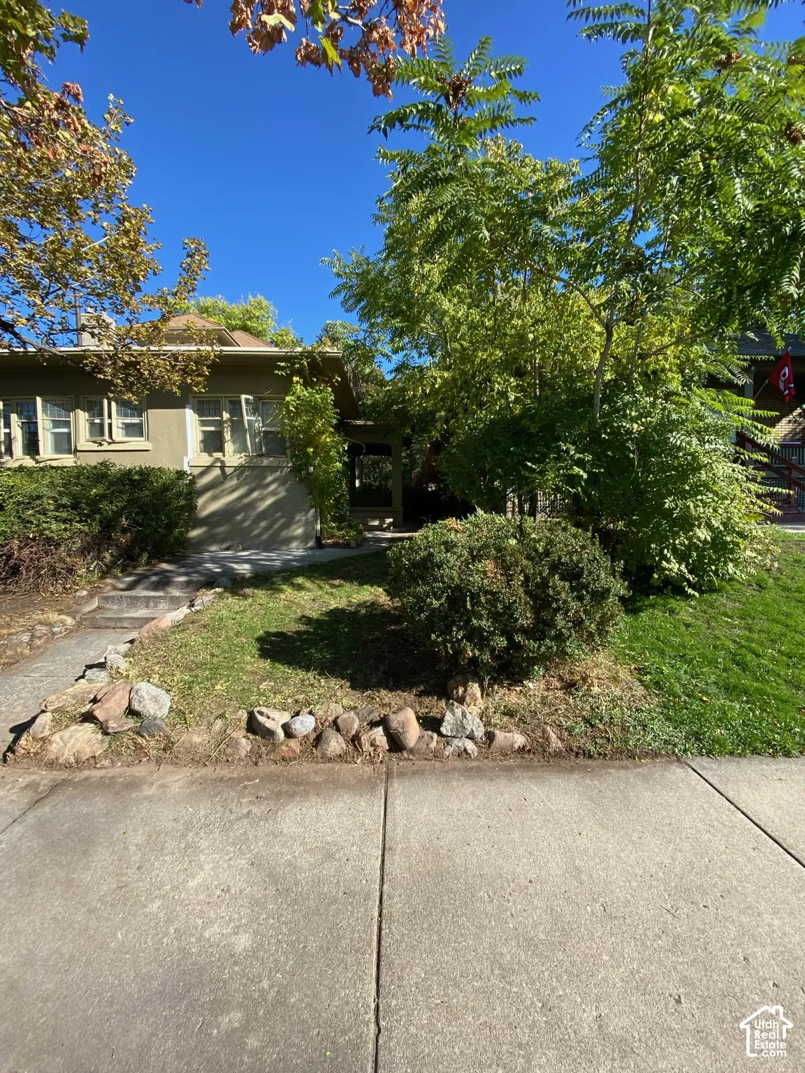 Exterior featuring stucco siding, multi-pane windows, stone landscape edging, and mature trees