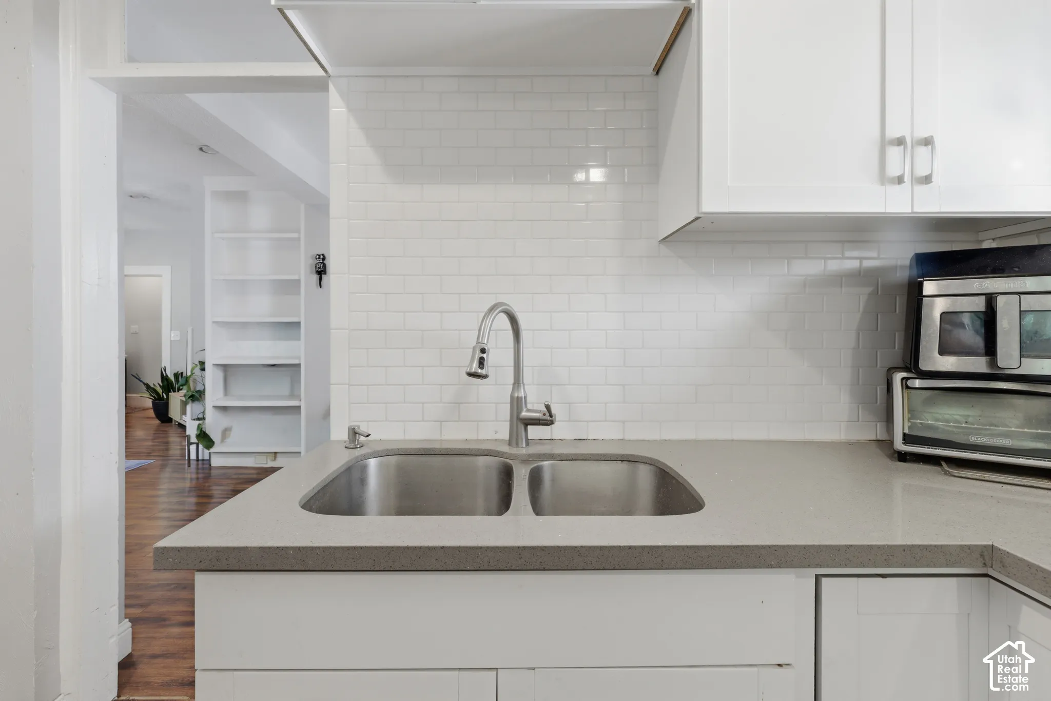 Kitchen featuring white shaker-style cabinetry, a stone-composite countertop, white subway tile backsplash, and a stainless steel double-basin sink with a pull-down faucet