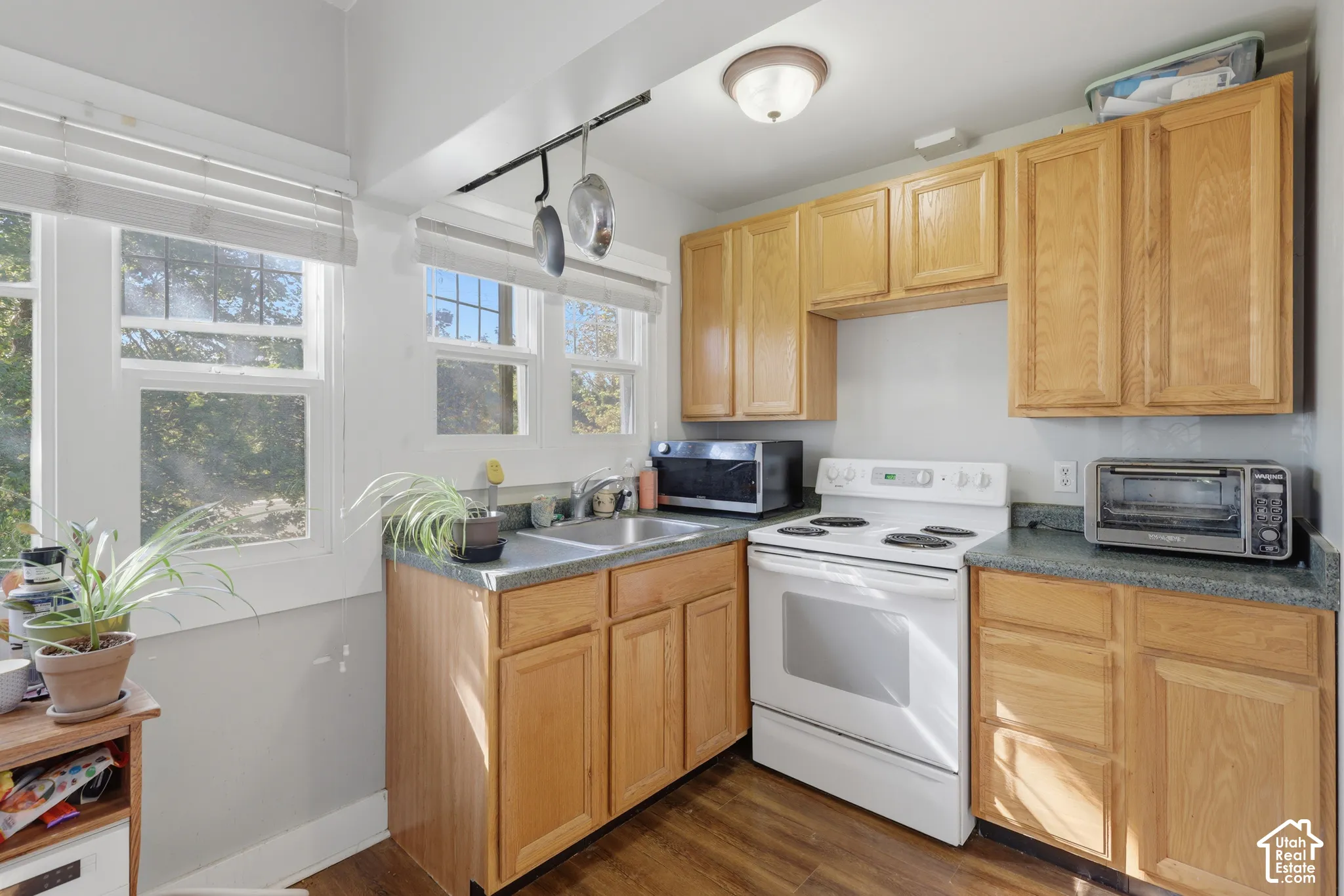 Kitchen featuring wood cabinetry, solid-surface countertops, wood-finish flooring, white freestanding range, and multiple windows