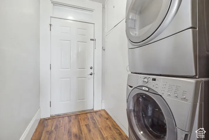 Laundry area featuring a stacked stainless steel washer and dryer, wood-finish flooring, and built-in cabinetry