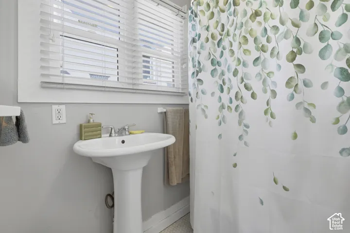 White pedestal sink with a dual-handle chrome faucet and horizontal slat window blinds