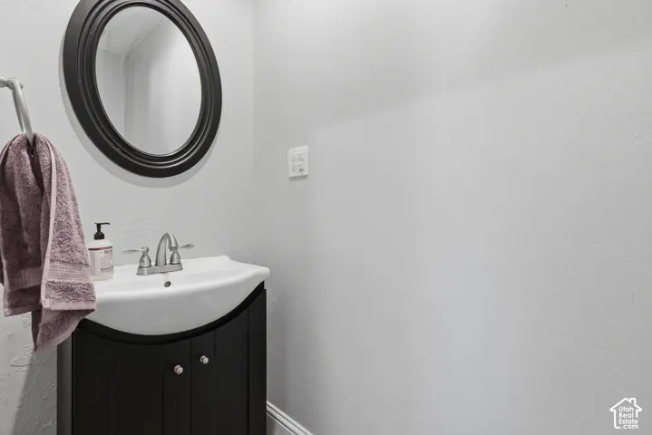 Curved black vanity cabinet with an integrated white sink, polished chrome dual-handle faucet, and matching oval wall mirror