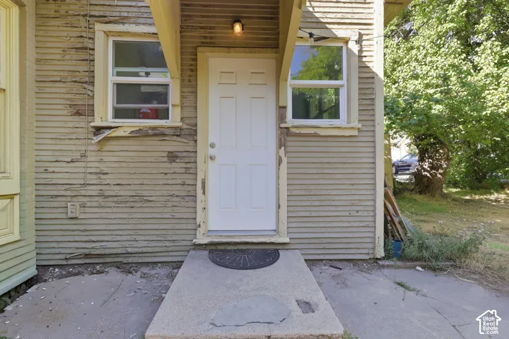 Exterior entryway featuring wood lap siding, a central six-panel door, two double-hung windows, and a concrete stoop