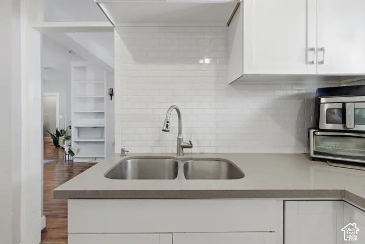 Kitchen featuring white shaker-style cabinetry, a stone-composite countertop, white subway tile backsplash, and a stainless steel double-basin sink with a pull-down faucet