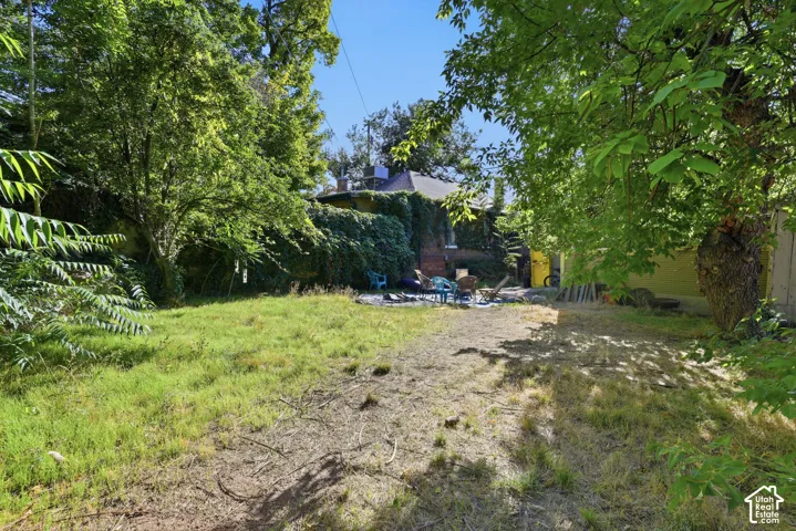 Backyard featuring a grass lawn, mature trees, and exterior brick masonry