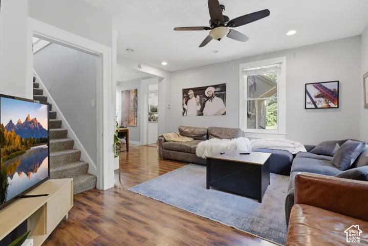 Living area featuring wood-finish flooring, recessed lighting, a ceiling fan with integrated light fixture, and large windows with casing trim