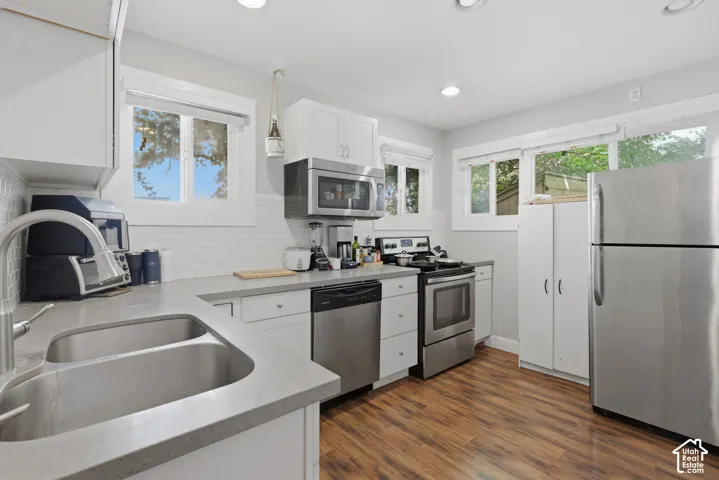Kitchen featuring white cabinetry, wood-finish flooring, stainless steel appliances, subway tile backsplash, and solid surface countertops with a dual-basin sink