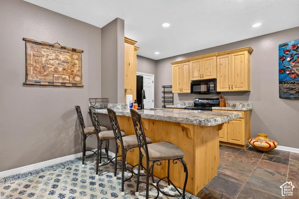 Kitchen featuring light-finish wood cabinetry, stone-patterned countertops, a center island with bar seating, and stone-tile flooring