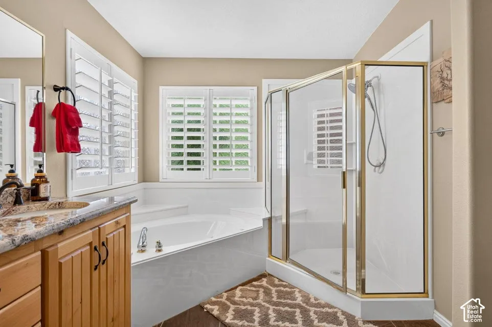 Bathroom featuring wood-finish cabinetry, stone countertop with integrated sink, corner jetted tub, and a glass-enclosed shower with metallic frame