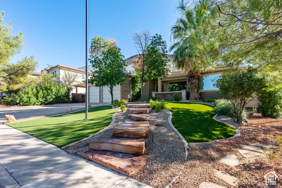 Single-story exterior featuring a stone-clad facade, attached garage, tiered natural stone staircase, and professional landscaping with artificial turf