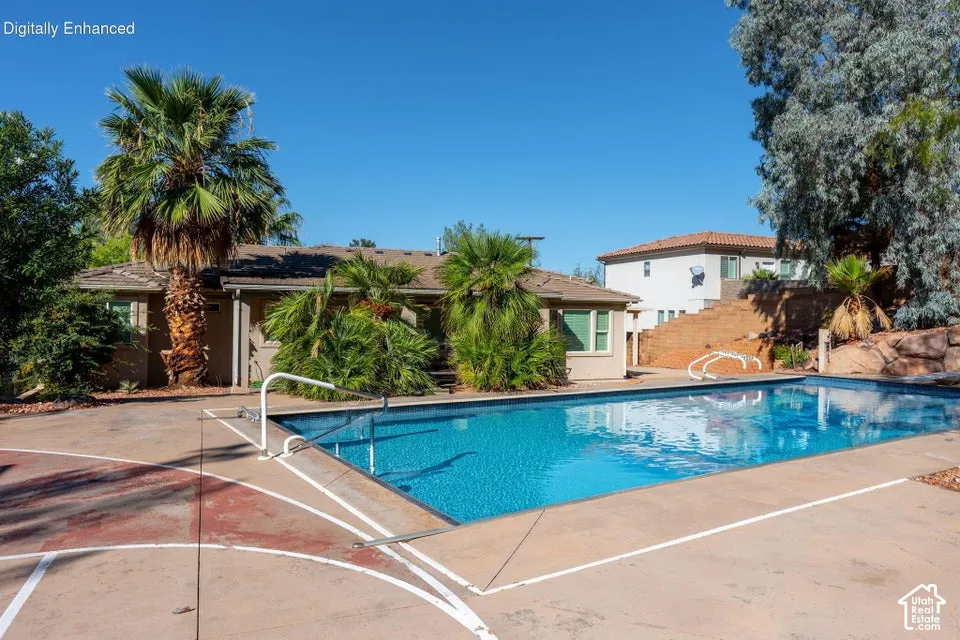 In-ground swimming pool with metal handrails, concrete patio hardscaping, and mature landscaping including palm trees