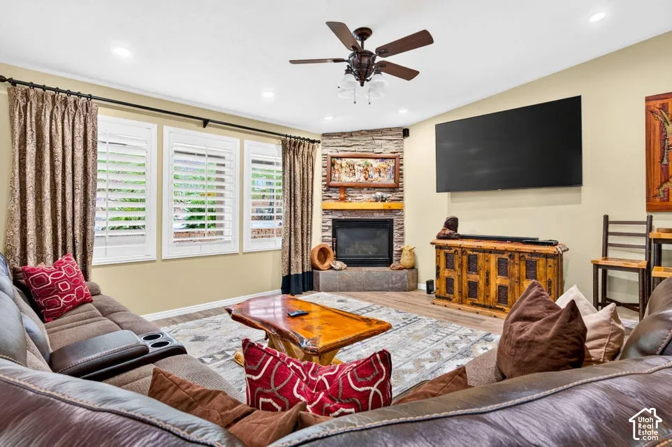 Corner fireplace featuring stone-veneer surround, wooden mantel, and raised hearth, complemented by wood-finish flooring, recessed lighting, and white plantation shutters