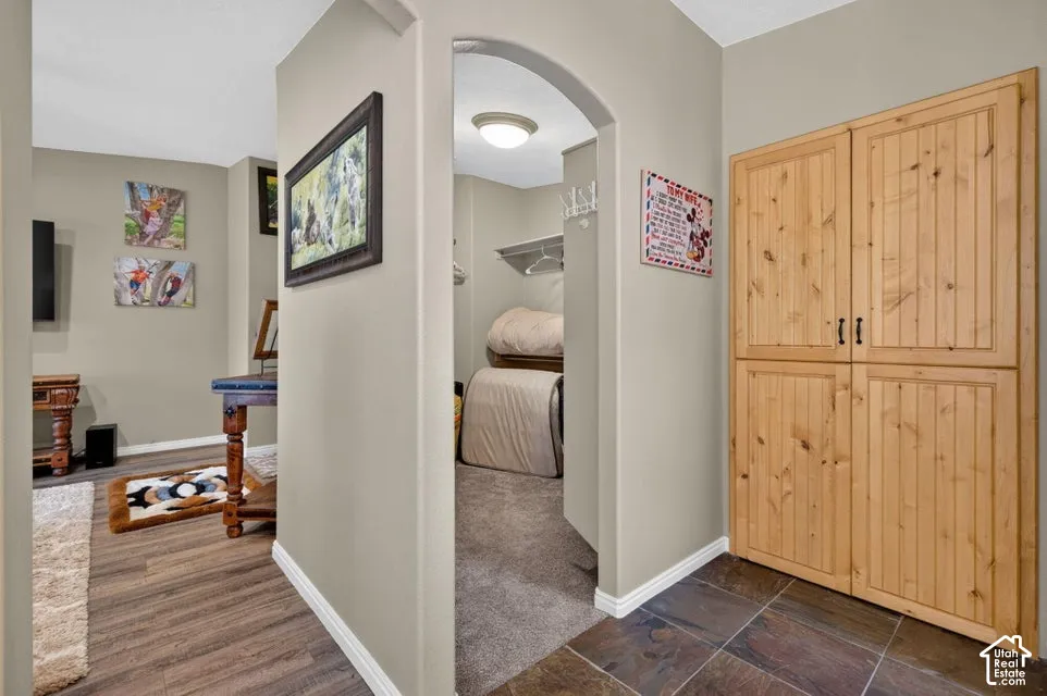 Arched entryway leading to a walk-in closet, wood-finish flooring, tile flooring, and floor-to-ceiling built-in natural wood cabinetry