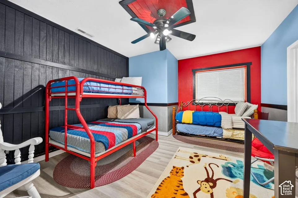Room featuring vertical paneling, wood-finish flooring, and a ceiling fan with integrated lighting