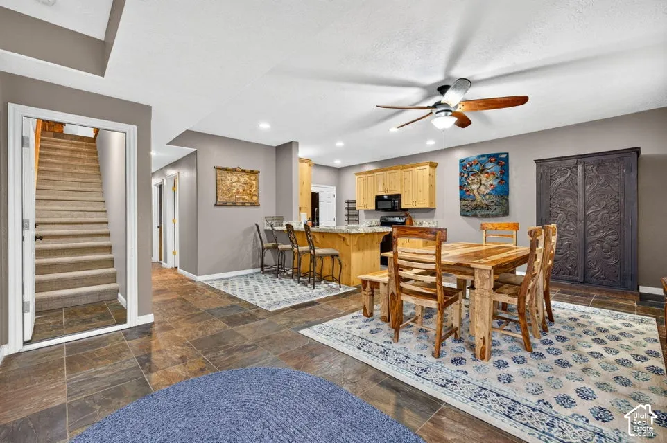 Open-concept interior featuring large-format tile flooring, light wood cabinetry, stone-surfaced kitchen island with bar seating, and a ceiling-mounted paddle fan