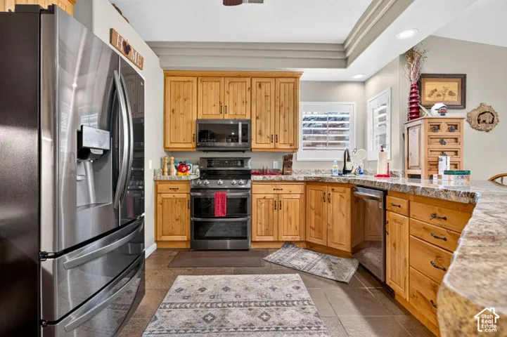 Kitchen featuring natural-finish wood cabinetry, stone-patterned countertops, stainless steel appliances, recessed ceiling lighting, and tile flooring