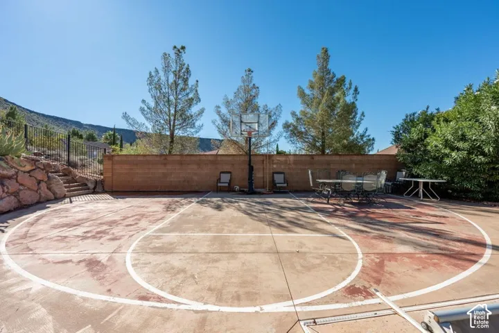 Concrete sports court featuring an integrated basketball hoop, enclosed by a masonry perimeter wall, rock-retaining wall, and metal fencing