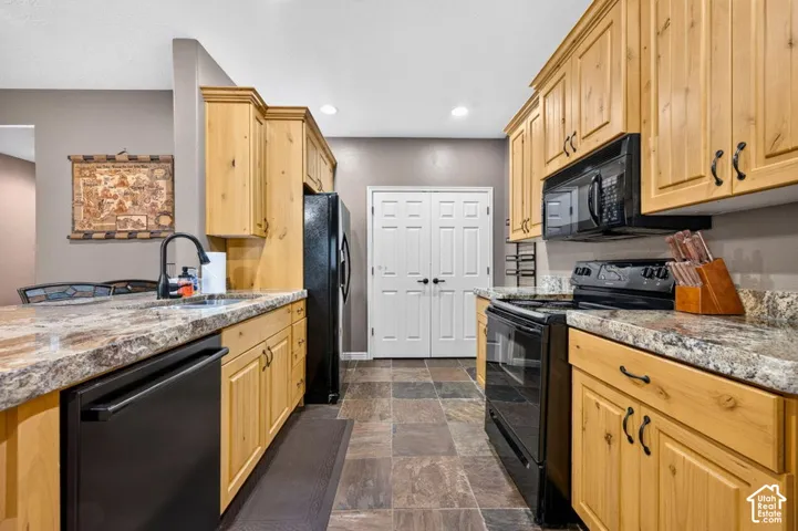 Kitchen featuring wood cabinetry, stone-finish countertops, stone-tile flooring, and black appliances