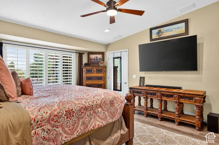 Vaulted ceiling, multi-panel bay window with plantation shutters, wood-finish flooring, and a ceiling fan with integrated lighting