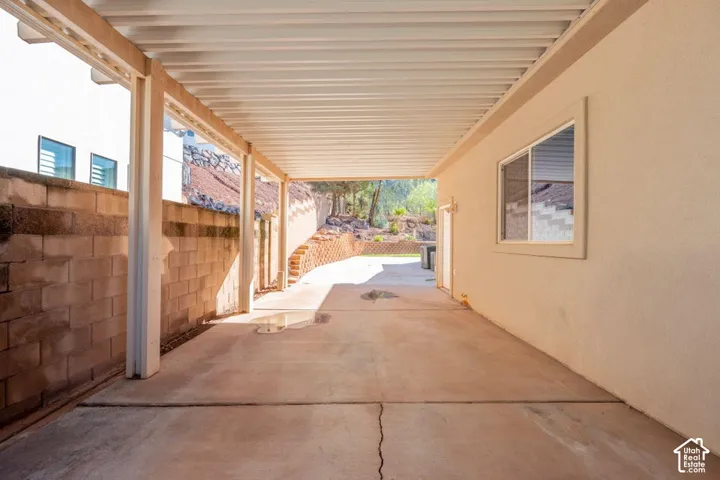 Covered concrete patio featuring a corrugated metal roof, support columns, and decorative masonry retaining walls