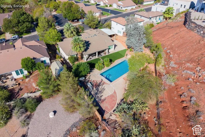 Aerial perspective of a property featuring an in-ground swimming pool, covered patio, artificial turf lawn, mature landscaping, and red rock terrain