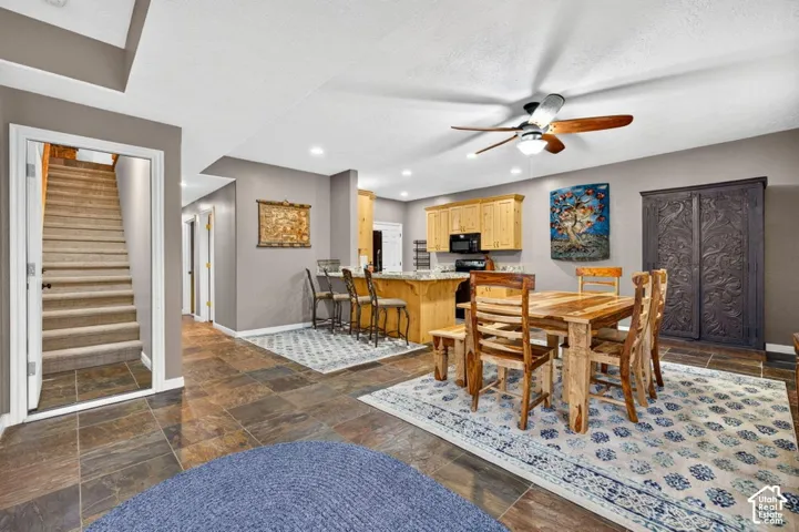 Open-concept interior featuring large-format tile flooring, light wood cabinetry, stone-surfaced kitchen island with bar seating, and a ceiling-mounted paddle fan