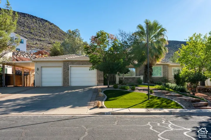 Single-story residence featuring a stone-veneer facade, two-car garage, covered side carport, and front landscaping with artificial turf and mature palm trees