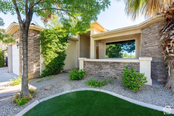 Single-story exterior featuring stacked stone veneer siding, an integrated garage, a concrete pathway, low-maintenance landscaping, and artificial turf