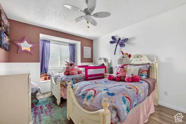 Bedroom featuring wood-finish flooring, a recessed window with a built-in bench seat, beadboard wainscoting, and a ceiling fan with integrated lighting