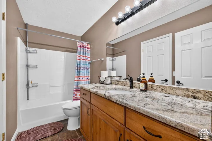 Bathroom featuring a stone-look countertop, wood-finish cabinetry, an undermount sink, a full-width vanity mirror, and a tiled tub-shower combination