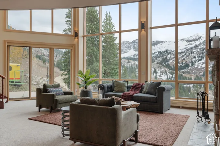 Floor-to-ceiling windows featuring mountain scenery, expansive wood-framed glazing, stone fireplace surround, and sliding glass doors