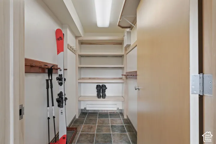 Storage area featuring custom wood shelving, dual wall-mounted wooden peg racks, and ceramic tile flooring