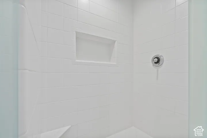 Shower enclosure featuring white square tile surround, built-in recessed wall niche, corner shelving, and circular chrome pressure-balance valve