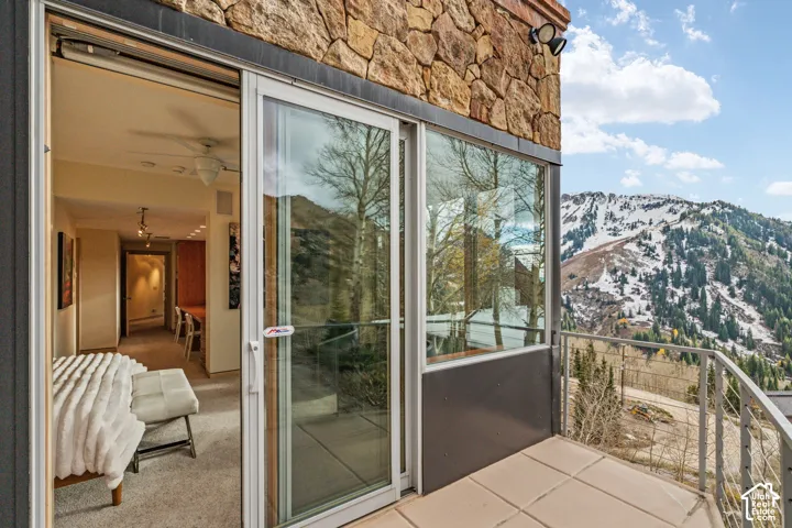 Exterior balcony with metal railing, stone-clad facade, and expansive glass sliding door leading to interior space with recessed lighting