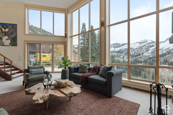 Floor-to-ceiling windows, double-height ceilings, mountain scenery, wall-mounted light fixtures, and staircase with wood treads